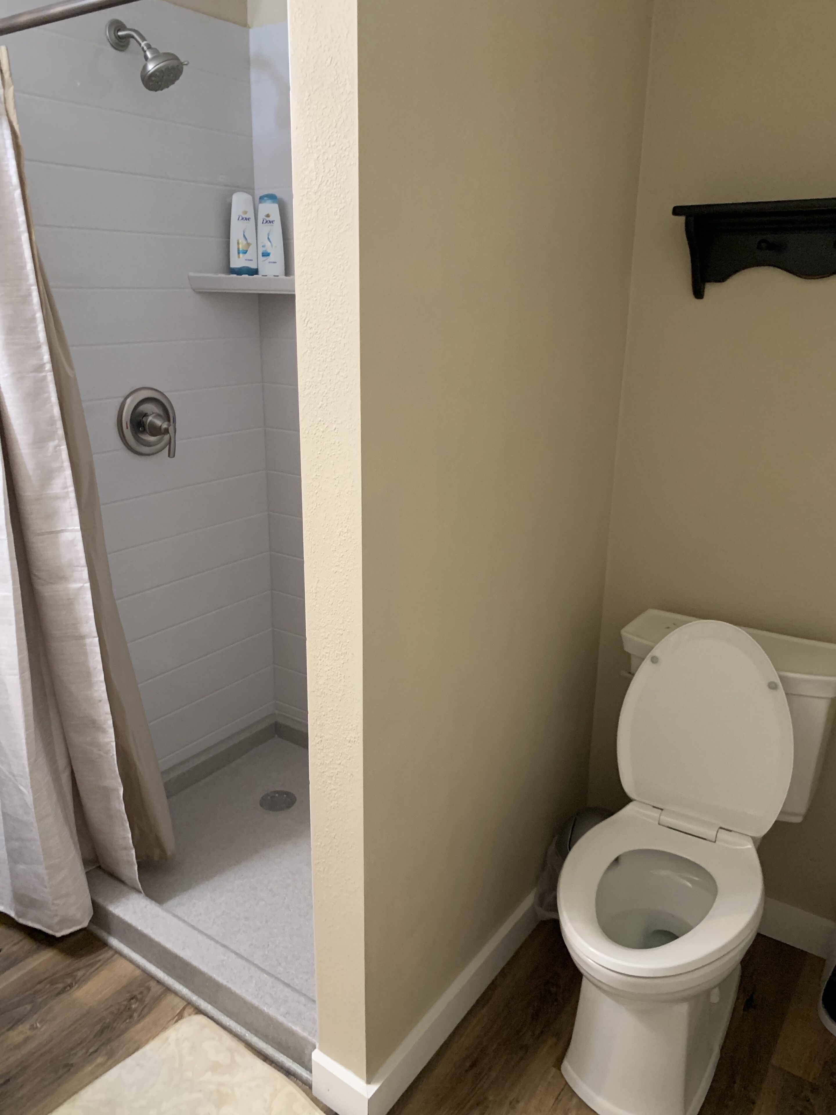 A bathroom with a shower, toilet, and a shelf with toiletries.
