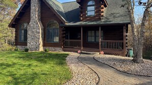 A log cabin with a stone chimney, a wrap-around porch, and a gravel pathway leading to the entrance. - Authentic Log Cabin Getaway w/Private Hot Tub (Berkeley Springs)