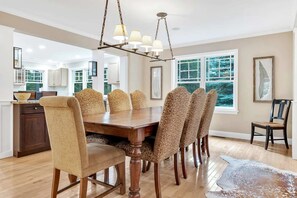 A dining room with a wooden table and patterned chairs, a chandelier, and a view of the outdoors through large windows. - Fairbanks Haven House with Hot Tub & Infrared Sauna (Quechee)