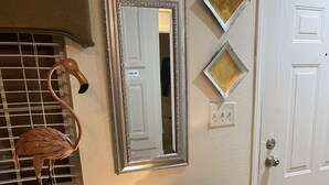 Una habitación con una mesita de consola de vidrio, un espejo y una puerta de marco blanco.