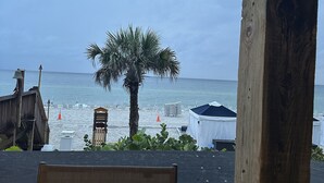 Vista de la playa con una mesa y sillas de madera, una palmera y sombrillas.