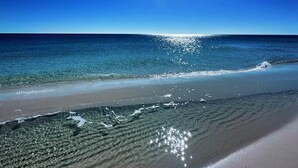 Una playa con agua cristalina, orilla arenosa y un sol brillante en el cielo.