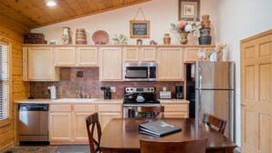 A wooden cabin-style kitchen with a dining table and chairs, equipped with a dishwasher, microwave, stove, and refrigerator. - Cozy-up in a Cabin for Two! (Branson)