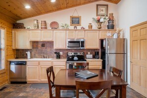 A wooden cabin-style kitchen with a dining table and chairs, equipped with a dishwasher, microwave, stove, and refrigerator.