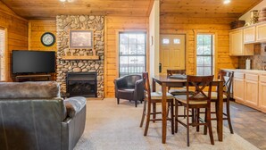 A cozy cabin interior with a stone fireplace, wooden walls, a dining area, and a television. - Cozy-up in a Cabin for Two! (Branson)