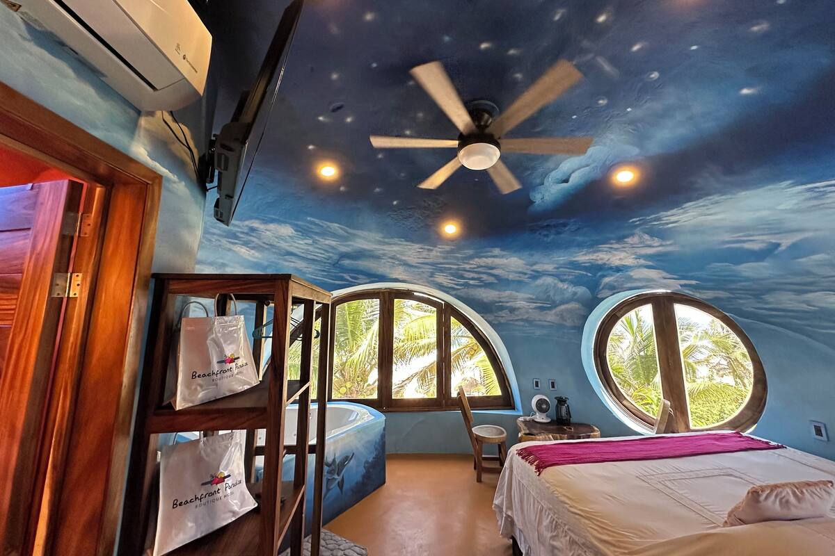 Quarto com mural no teto, cama, escrivaninha e janela.