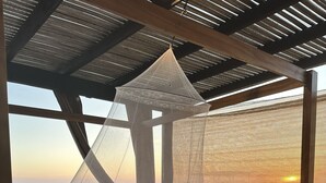 Una cama con dosel, ropa de cama estampada y vista al mar al atardecer.