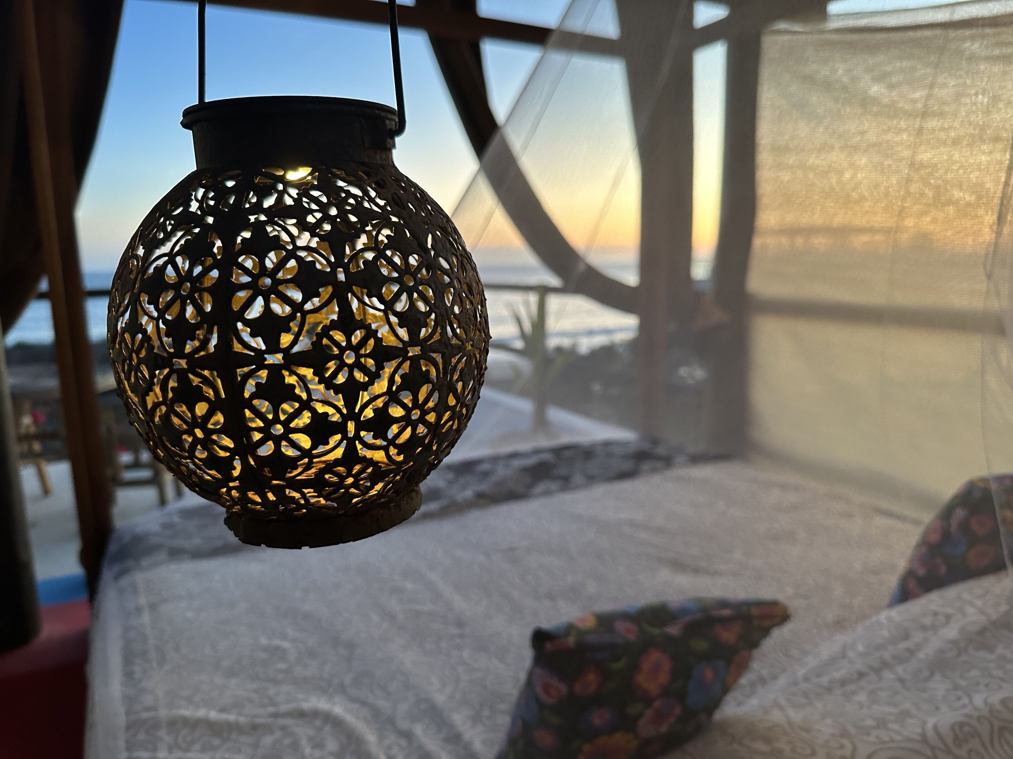 Un farol colgante con intrincados diseños recortados, una cama con cubrecama blanco texturizado y vistas a un paisaje nevado a través de una ventana.