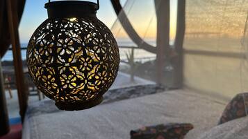 Un farol colgante con intrincados diseños recortados, una cama con cubrecama blanco texturizado y vistas a un paisaje nevado a través de una ventana.
