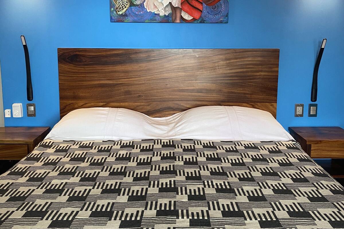 Uma cama com colcha estampada, cabeceira de madeira e um quadro acima.