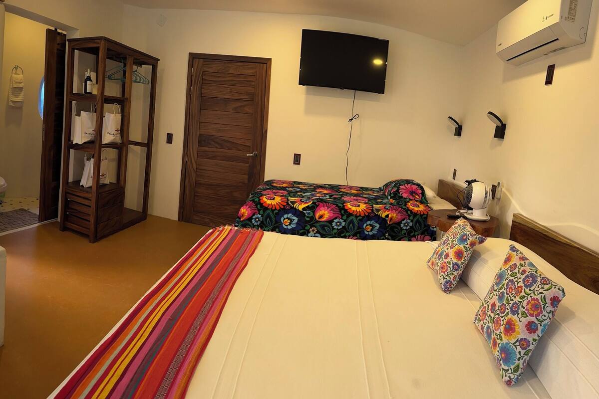 Quarto com banheira, cama com roupa de cama floral, guarda-roupa e televisão fixada na parede.