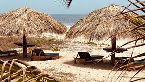 Una playa con sombrillas de paja y sillas de madera para tomar el sol.
