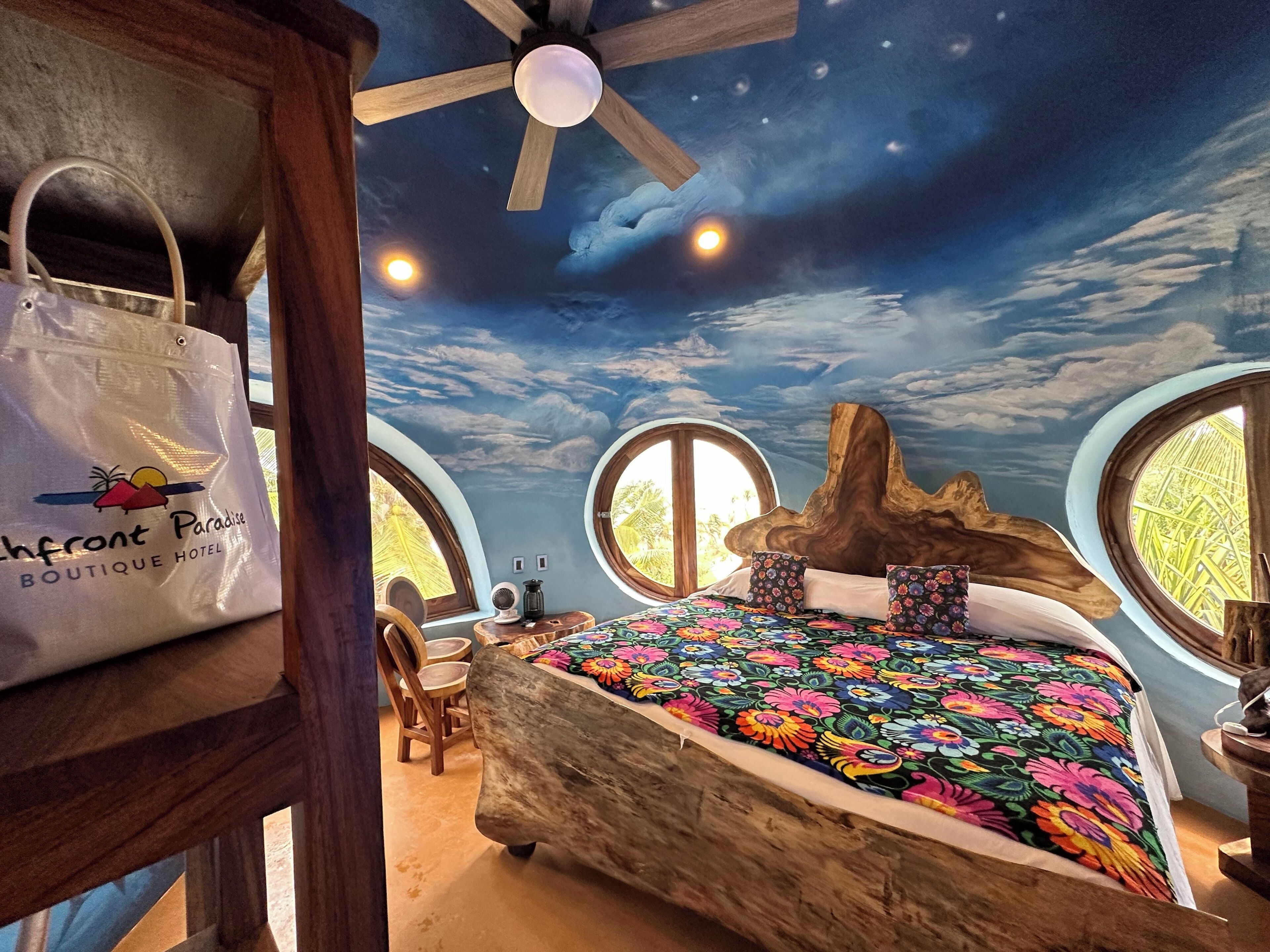 Een slaapkamer met een bed, een plafondventilator en uitzicht op de lucht door ronde ramen.