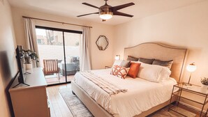 A bedroom with a bed, bedside tables, a ceiling fan, and a view through a sliding door. - Stylish, Remodeled Condo - Pool, Tennis, Golf - (Palm Springs)