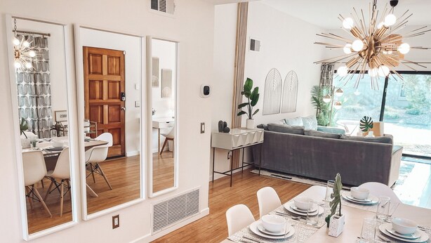 A modern dining area with a wooden table set for four, large mirrors on the wall, and a view of the outdoors. - Stylish, Remodeled Condo - Pool, Tennis, Golf - (Palm Springs)