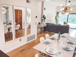 A modern dining area with a wooden table set for four, large mirrors on the wall, and a view of the outdoors. - Stylish, Remodeled Condo - Pool, Tennis, Golf - (Palm Springs)