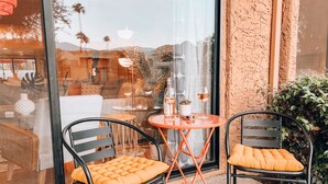 An outdoor seating area with two chairs and a table, a window with reflections, and a textured wall. - Stylish, Remodeled Condo - Pool, Tennis, Golf - (Palm Springs)