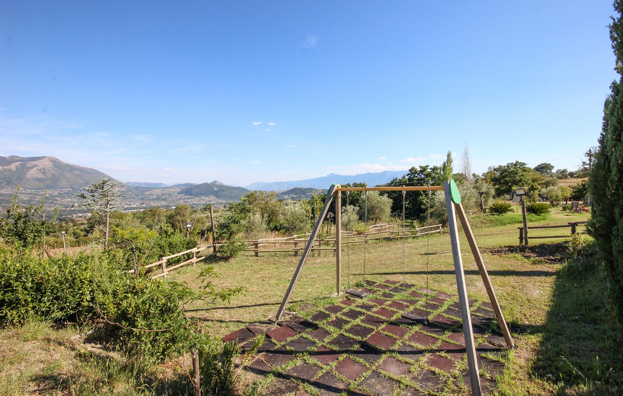 Une balançoire installée dans un espace verdoyant, avec vue sur des montagnes lointaines et un ciel dégagé.