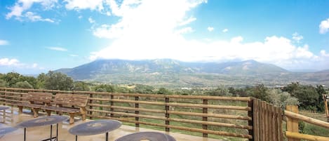 An outdoor seating area with tables and chairs, a wooden fence, and a view of a mountain range.