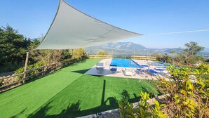 Une piscine sur le toit offrant une vue sur les montagnes, entourée de gazon artificiel verdoyant et de chaises longues.
