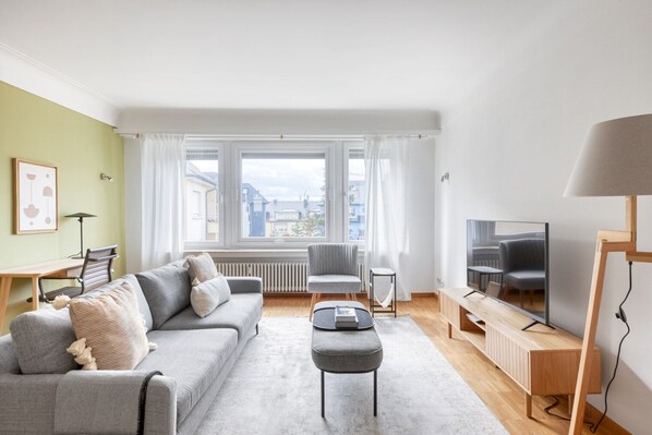 A modern living room with a grey sofa, a small table, a TV, and a lamp. - Sleek Limpertsberg 2BR w/ Balcony, nr Bus Station, by Blueground (Luxembourg)