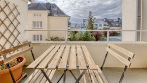 Un balcón con mesa y sillas de madera, una planta en maceta y vistas a edificios cercanos.