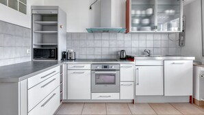 Una cocina moderna con armarios blancos, estufa de acero inoxidable, microondas y un armario con puerta de vidrio sobre el fregadero.
