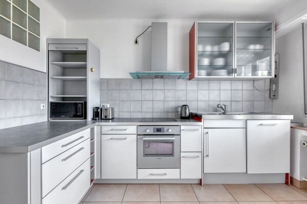 Una cocina moderna con armarios blancos, estufa de acero inoxidable, microondas y un armario con puerta de vidrio sobre el fregadero.