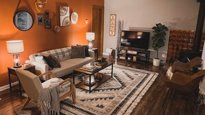 Un salon chaleureux avec un canapé, une table basse et un téléviseur. Les murs sont décorés et il y a une plante dans un coin.