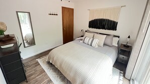 Une chambre à coucher comprenant un lit, un ventilateur de plafond, une table de chevet, une commode, un meuble à tiroirs, un miroir et une fenêtre.