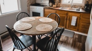 Une table à manger avec quatre sets de table en fibres tressées, des chaises noires, un buffet en bois, une cuisinière et une fenêtre.
