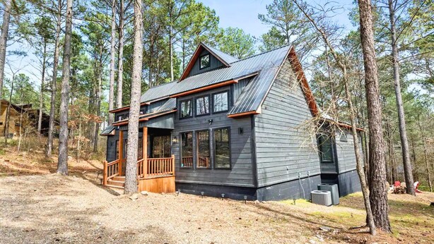 Une cabane dotée d’une terrasse en bois, de grandes fenêtres et d’un toit en métal, entourée de grands pins.