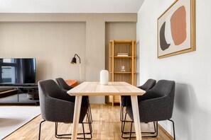 Un soggiorno moderno con un tavolo da pranzo in legno, due poltrone grigie, una libreria e una TV.