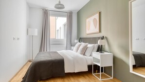 A modern bedroom with a bed, bedside table, lamp, and a large mirror.