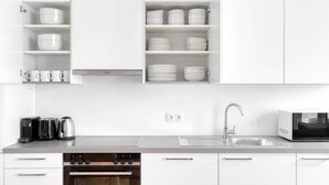 A modern kitchen with white cabinetry, a built-in oven, a microwave, and a coffee maker.