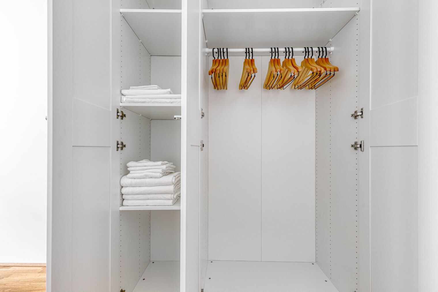 A white wardrobe with shelves for folded clothes and a hanging rod with wooden hangers.