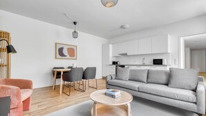 A modern living room with a grey sofa, a round coffee table, and a dining area with a wooden table and grey chairs.