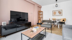 A modern living room with a flat-screen TV, a coffee table, a bookshelf, and a dining area with chairs and a table. - Luxe Mariahilf 2BR w/ Elevator, near Mariahilfer Straße (Vienna)