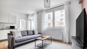 A modern living room with a grey sofa, a coffee table, a flat-screen TV, and large windows with white curtains. - Luxe Mariahilf 2BR w/ Elevator, near Mariahilfer Straße (Vienna)