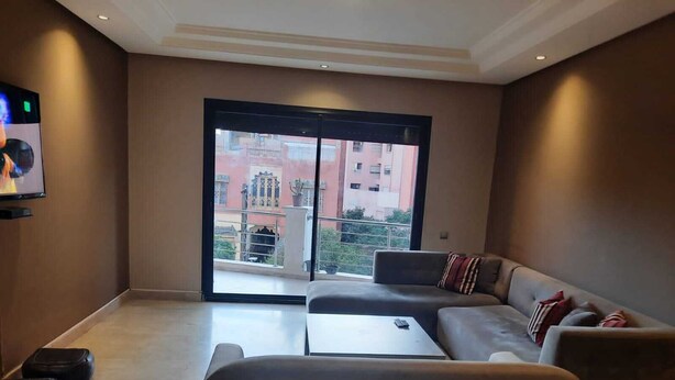 A spacious living room with a large sliding glass door leading to a balcony, a sofa, a coffee table, and a television on the wall. - Torque 111 (Marrakech)