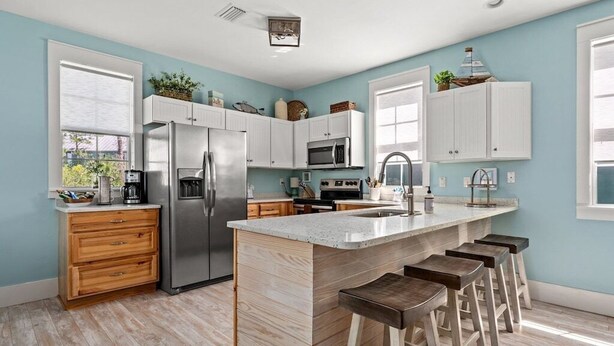 Una cocina moderna con una isla central, taburetes de bar y armarios blancos.
