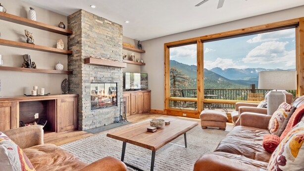 Un salon spacieux avec une cheminée en pierre, des étagères en bois et une grande fenêtre donnant sur une vue imprenable sur les montagnes.