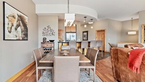 Un espace repas moderne avec une table et des chaises en bois, une cuisine en arrière-plan et un coin salon confortable avec un canapé marron.