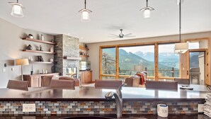 Une cuisine moderne dotée d’un grand îlot central, d’étagères en bois et offrant une vue sur les montagnes.