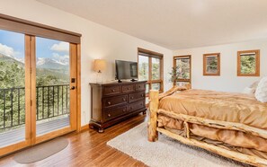 A bedroom with a wooden bed, a dresser, a television, and a balcony with a mountain view. - Alpenglow Vacation Home at Windcliff (Estes Park)
