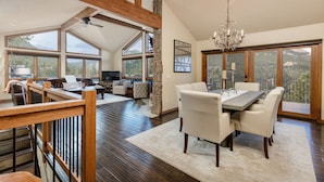 A spacious living area with a high ceiling, large windows, and a dining area with a chandelier.
