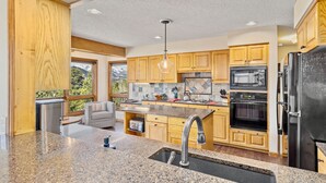 A modern kitchen with granite countertops, wooden cabinets, a stainless steel refrigerator, and a built-in oven.