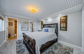 A bedroom with a large bed, a wooden headboard, a patterned rug, and artwork on the walls.