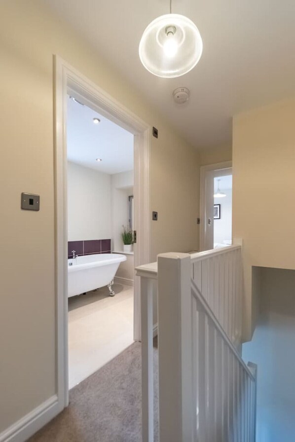 A hallway leading to a bathroom with a white bathtub and a modern light fixture. - Two Ways, Tansley, near Matlock (Derbyshire)