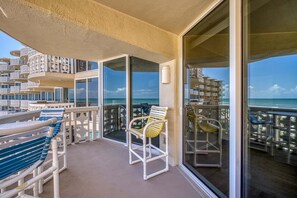 A balcony with a view of the ocean, white outdoor furniture, and a glass door leading to another area. - Oceanfront Condo with Private Balcony Heated Pool and Walk to Flagler Avenue (New Smyrna Beach)